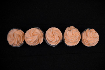 Five cupcakes on a black background with orange cream. View from above. Cake in one line.