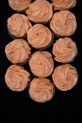 Close-up of many cupcakes on a black background. Orange cream. View from above.