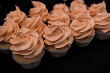 Close-up of many cupcakes on a black background. Orange cream. At an angle.