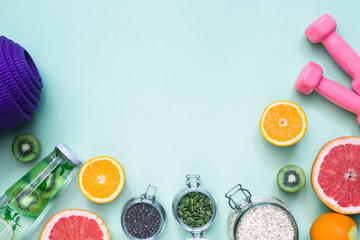 Food for fitness, healthy lifestyle frame flat lay with fresh fat burning fruits orange and grapefruits slices, complex carbohydrates, detox water bottle, pink hand weights, light green background