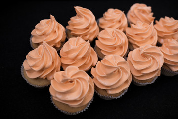 Close-up of many cupcakes on a black background. Orange cream. At an angle.