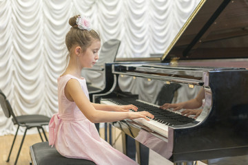 Fototapeta na wymiar girl in a beautiful pink dress playing on a black grand piano. Girl playing on a black piano.