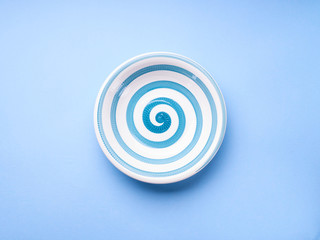 Ceramic Dish with hypnotizing spiral on pastel blue background. Minimal concept