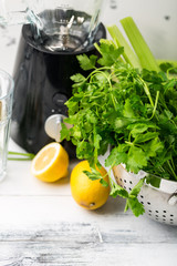 Green cocktail smoothie parsley celery lemon lime slices, healthy drink ingredients, glass of beverage on white wooden table, detox diet clean eating, with cocktail maker blender vegetables on table