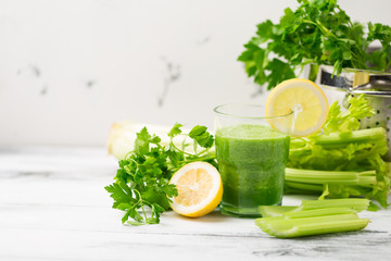 Green cocktail smoothie parsley celery lemon lime slices, healthy drink ingredients, glass of beverage on white wooden table, detox diet clean eating, with vegetables on table