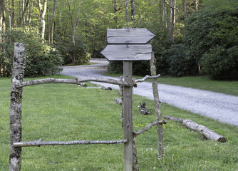 Rustic Signs on Post with Wooden Logs in front of  Grass, Dirt Road and Forest