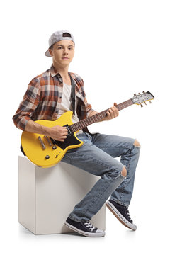 Teenager with an electric guitar sitting on a cube and playing