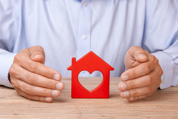 Concept home insurance, protection from burglary or destruction. The man with his hands fences the house like fence, covers, the heart inside.