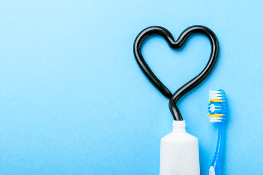Black toothpaste from charcoal for white teeth. Tooth-paste in the form of heart, tube and toothbrush on blue background. Copy space for text