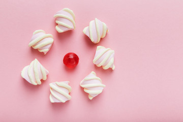 Marshmallows and red candy on pink background