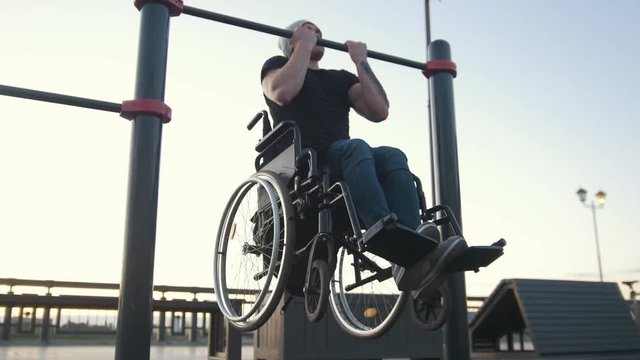 Young disabled man in wheelchair engaged on the crossbar outdoors