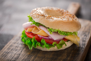Sesame bagel sandwich with lettuce, tomato, yellow cheese and ham.