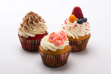 Cupcakes with white cream decorated with berries, roses and chocolate chips on white background