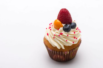 Cupcake with white cream decorated with strawberry and blueberry on white background