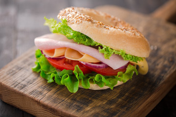 Sesame bagel sandwich with lettuce, tomato, yellow cheese and ham.