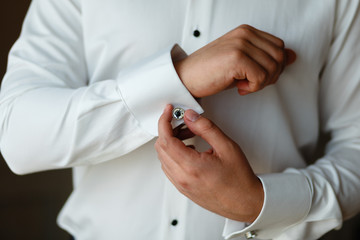 Obraz na płótnie Canvas Close-up hands of man buttons cuff link on French cuffs sleeves luxury white shirt. The groom is preparing for the wedding, going to meet with the bride. Hands of wedding groom getting ready in suit