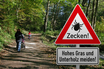 Schild mit Zeckenwarnung in Risikogebiet im Naturpark - mit Familie beim Spaziergang