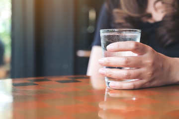 Closeup image of woman's hand holding a glass of cold water on table