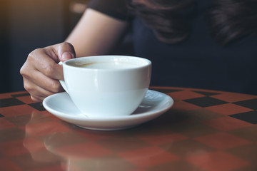 Closeup image of a woman holding and drinking hot coffee in cafe