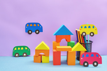 Toy cars made of cardboard and toy houses made of cubes on a pink background