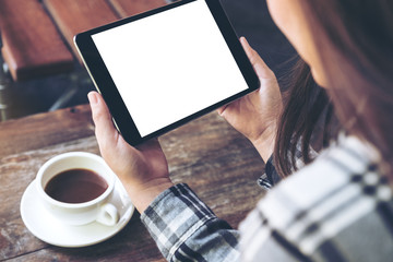 Mockup image of a woman holding black tablet pc with white blank screen with coffee cup on table background