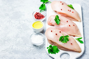 raw chicken breasts on cutting board with herbs,oil,tomatoes. Selective focus, copy space.