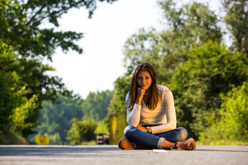 Portrait einer jungen sitzenden Frau auf einer Straße im Sommer