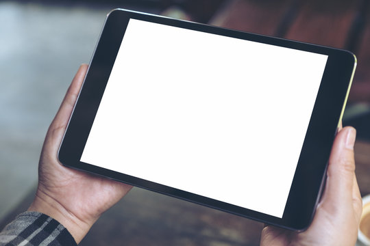 Mockup image of hands holding black tablet pc with blank white desktop screen in cafe