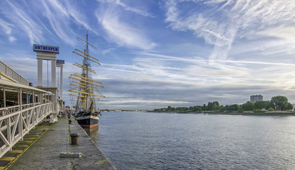 ANTWERP, BELGIUM - 25 JUNE, 2017: Promenade and pier in Antwerp with signs 'Anwerpen' Antwerp in dutch Railings, benches, poles and a large sailing ship in the background.