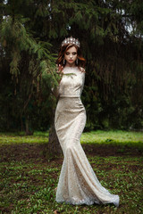 Fototapeta premium Beautiful model wearing glamour golden dress and crown is posing in the forest
