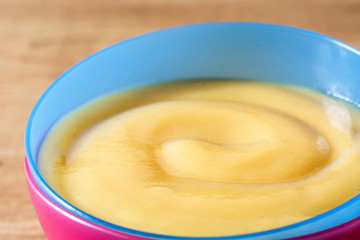 Baby food: colorful bowl of fruit puree on wooden table. Close up
