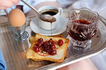 Breakfast in bed in hotel. Hand of woman spreading cherry jam on a toast.