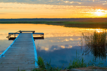 Fototapeta na wymiar orange sun at sunset over a picturesque lake with a beautiful wooden pier