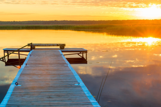 horizontal picture of a beautiful landscape - a long wooden pier and the setting sun over a picturesque lake