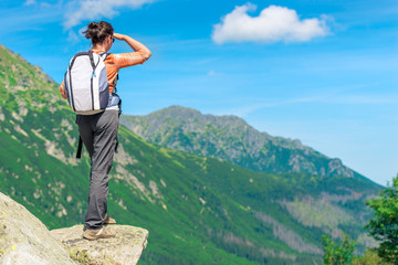 Obraz premium a tourist with a backpack in the mountains on a precipice looking into the distance to the mountains, the view from the back