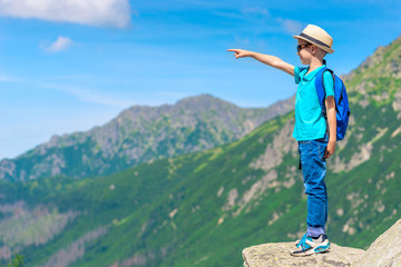 Fototapeta na wymiar portrait of a boy traveler standing on a rock and pointing at a mountain