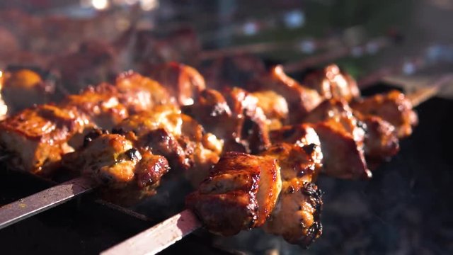 Appetizing delicious fried pieces of meat on skewers are roasted on a large grill in the open air. The chef prepares a barbecue. slow motion