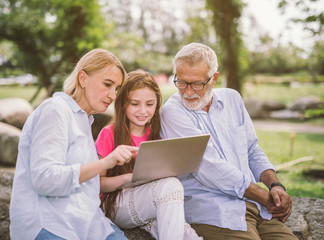 Fototapeta na wymiar Grandfather And Grandchildren family using laptop while resting in park