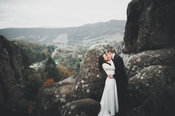 Naklejka premium Wedding couple in love kissing and hugging near rocks on beautiful landscape