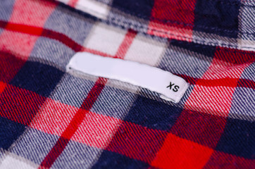 Size XS textile clothes label tag on cage red blue white cotton background