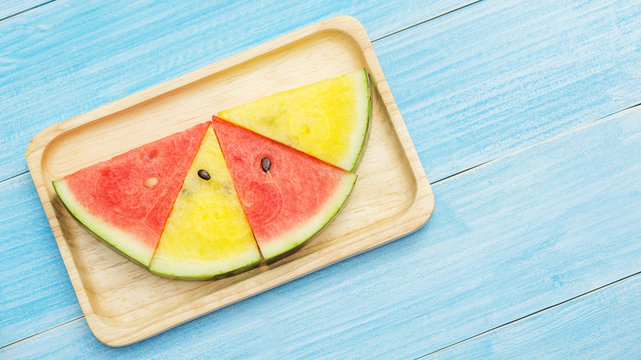 Red and yellow watermelon on a plate and blue wooden table.