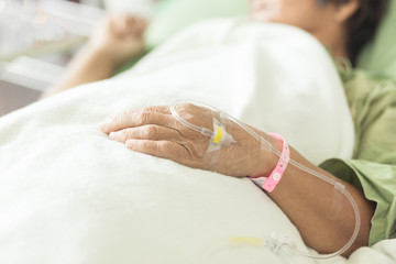 Fototapeta na wymiar Selective focus Hand of the old woman lying on the bed with IV line on hand in the patient room in color tone.