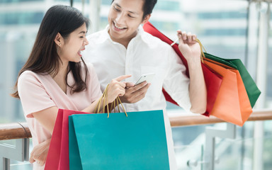 Young woman and man holding  colorful shopping bags while using a mobile phone in the mall.