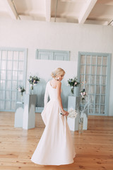 Beautiful bride in front of wedding arch with flowers and decor. Bouquet in the hands and details. The girl is happy, smiling and dancing. Dream wedding dress in modern style