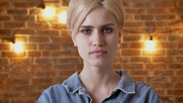 Young attractive hipster girl is watching at camera, brick background