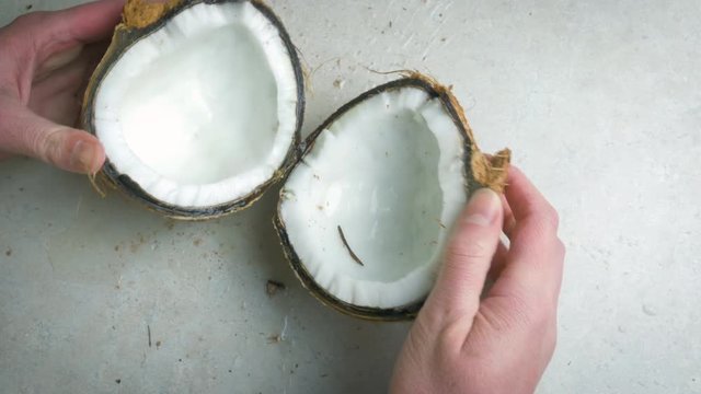 Woman pries open coconut halves in 4k. Top down view as the woman breaks open the shell of the tropical nut releasing coconut water over the kitchen counter. Shot represents healthy vegan eating.