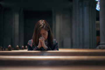 A Christian girl is sitting and praying with broken heart in the church.