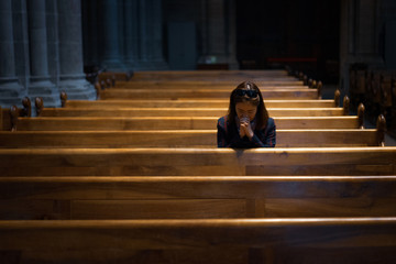A Christian girl is sitting and praying with broken heart in the church. - obrazy, fototapety, plakaty