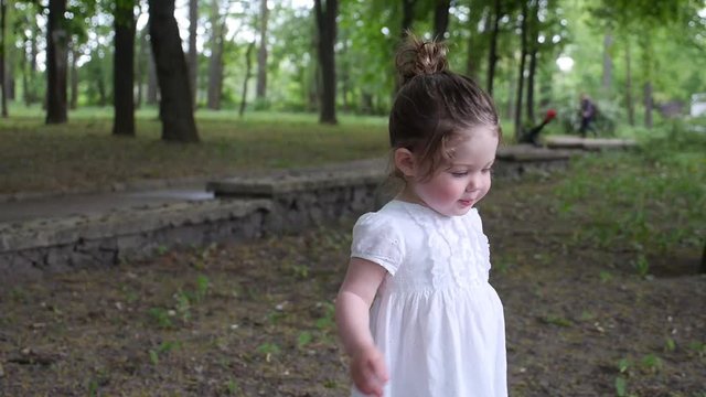 A little girl walks in a green park with her mother