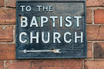 metal and enamel street sign on brick wall stating to the baptist church with arrow pointing to the left